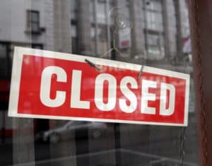 Closed sign in a shop showroom with reflections - red sign over desaturated background